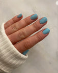 Hand with nails painted in soft blue shade using Sky - Clean Nail Polish, showcasing a smooth, glossy finish on natural nails against a light background.