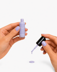 Close-up of hands with violet nail polish applied, holding an open bottle and brush applying a drop, showcasing Clean Pocket Nail Polish Duo - Violet in a smooth, creamy texture.