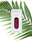 Sangria - Clean Nail Polish bottle in deep red shade displayed in white HOOPLA packaging set against green palm leaves background, emphasizing clean beauty and vegan nail polish.