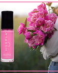 Bright pink nail polish bottle labeled HOOPLA next to a person holding a bouquet of vibrant pink flowers, highlighting Pink Flamingo - Clean Nail Polish in a natural outdoor setting.
