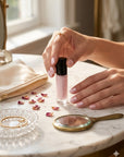 Close-up of hands with neatly manicured nails holding a bottle of Stargazer - Clean Nail Polish on a marble surface with dried rose petals, a small mirror, and jewelry nearby, highlighting a clean beauty nail treatment.