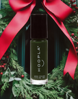 Holly - Clean Nail Polish bottle with dark green shade displayed in front of a festive holiday wreath decorated with red berries and a large red bow, showcasing a clean beauty vegan nail treatment.