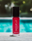 A small bottle of Pink Foil - Clean Nail Polish by HOOPLA, featuring a vibrant pink foil color with a black cap, placed on a wooden surface with a blurred outdoor background.