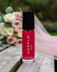 HOOPLA Pocket Nail Polish - Blissful - vegan, cruelty free, made in the USA in a vibrant pink shade with a black cap, placed on a wooden surface with a soft pink fabric and blurred flowers in the background.