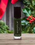 A green nail polish bottle with a black cap labeled Hoopla, set on a wooden surface with festive holiday greenery and red berries in the background, representing Holly - Clean Nail Polish.