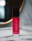 A vibrant red nail polish bottle with a black cap displayed on a marble surface, showcasing the Pink Foil - Clean Nail Polish for a clean beauty nail treatment.