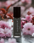 A bottle of Diesel - Clean Nail Polish in a muted green shade, surrounded by soft pink cherry blossoms and delicate red leaves, highlighting a natural and clean beauty vibe.