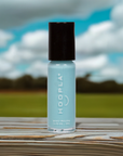 Bottle of Sky - Clean Nail Polish in a soft blue shade on a wooden surface with a blurred outdoor background featuring green grass and a cloudy blue sky.