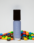 M+M - Clean Nail Polish bottle in light lavender shade standing upright surrounded by colorful candy pieces on a white background, showcasing clean beauty nail treatment.
