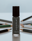 Close-up of a grey nail polish bottle labeled "HOOPLA" with a black cap, surrounded by assorted colored pencils, promoting Diesel - Clean Nail Polish.