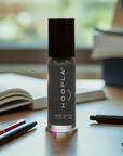A small bottle of HOOPLA mini-polish in a dark gray shade standing on a wooden desk surrounded by books and pens, highlighting clean beauty and nail treatments with Diesel - Clean Nail Polish.