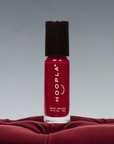 A bottle of Velvet - Clean Nail Polish in vibrant red with a black cap, standing upright on a textured velvet surface, highlighting a clean beauty nail polish option.