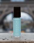 Close-up of a light blue nail polish bottle labeled "HOOPLA" standing on a stone surface with a blurred outdoor background, showcasing the product Sky - Clean Nail Polish.
