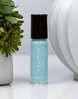 Small bottle of Sky - Clean Nail Polish in light blue shade with black cap, placed on white surface between green plant and white decorative object, showcasing clean beauty nail polish.