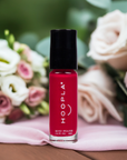 HOOPLA Pocket Nail Polish - Blissful - vegan, cruelty free, made in the USA in a vibrant red shade displayed with soft pink and white roses in the background.