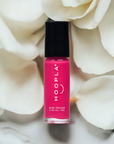 Bottle of Rosy - Clean Nail Polish in vibrant pink shade resting on soft white rose petals, highlighting clean beauty and vegan-friendly nail treatment.