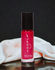 Bottle of HOOPLA brand red nail polish named Private School Girl - Clean Nail Polish standing on a reflective surface with a white silky cloth in the background, showcasing clean beauty and nail treatment attributes.