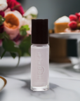 A small bottle of Angel - Clean Nail Polish with a black cap, positioned on a marble surface with blurred flowers and a dessert in the background, conveying a clean beauty and vegan nail polish concept.