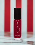 Red nail polish bottle with black cap against a red and white striped background featuring the product Velvet - Clean Nail Polish by Hoopla.
