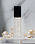 Bottle of Mini Pearl - Clean Nail Polish with a soft pearlescent white shade, surrounded by scattered pearls on a smooth white surface, conveying elegance and clean beauty.