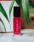 Bottle of Pink Foil - Clean Nail Polish by HOOPLA with vibrant pink shimmer, placed among green leaves, highlighting vegan, clean beauty nail treatment.