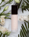 Fluff - Clean Nail Polish in a soft pink shade by HOOPLA, surrounded by delicate white flowers and green leaves, highlighting a natural and clean beauty nail treatment.