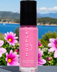 Pink Flamingo - Clean Nail Polish bottle in bright pink shade displayed among vibrant pink flowers with a scenic blue lake and forested hills in the background.