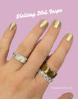 Hand with nails painted in shiny metallic gold polish showcasing Gold Foil - Clean Nail Polish, styled with silver, gold, and crystal rings on a lavender background.