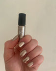 Hand holding a bottle of Gold Foil - Clean Nail Polish with nails painted in a shimmering gold foil finish, showcasing a clean beauty nail polish option.