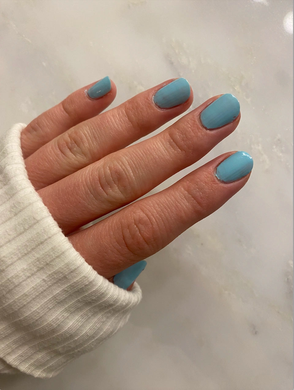 Hand with nails painted in soft blue shade using Sky - Clean Nail Polish, showcasing a smooth, glossy finish on natural nails against a light background.